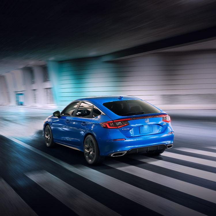 Rear driver-side view of the 2022 Honda Civic Sport Touring Hatchback in Boost Blue Pearl, driving through a tunnel.